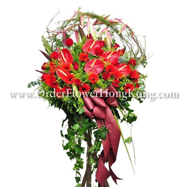 Vibrant bouquet with red flowers, greenery, and a decorative ribbon on a wooden stand.
