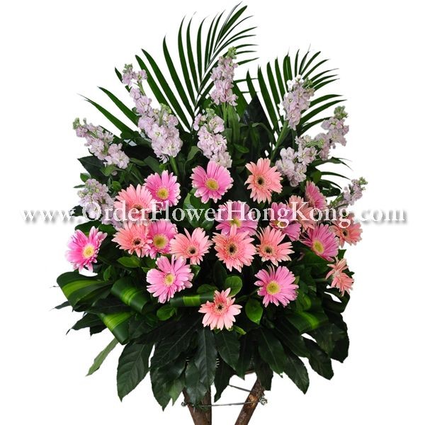 Floral arrangement with pink gerbera daisies, white flowers, and green palm leaves.