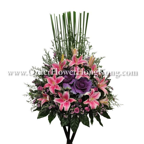 Floral arrangement with pink lilies, purple flowers, and tall green leaves on a white background.
