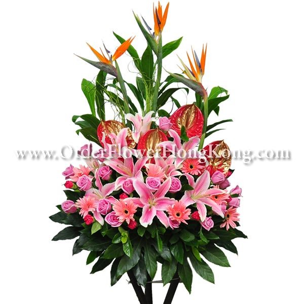 Floral arrangement with pink lilies, roses, orange bird of paradise, and green leaves.