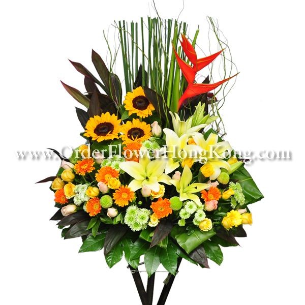 Vibrant floral arrangement with sunflowers, lilies, and tropical leaves on a white background.