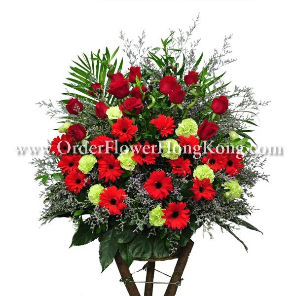 Floral arrangement with red roses, red gerberas, green carnations, and lush greenery.
