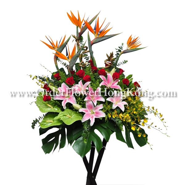 Floral arrangement with pink lilies, red roses, orange bird of paradise, and green leaves.