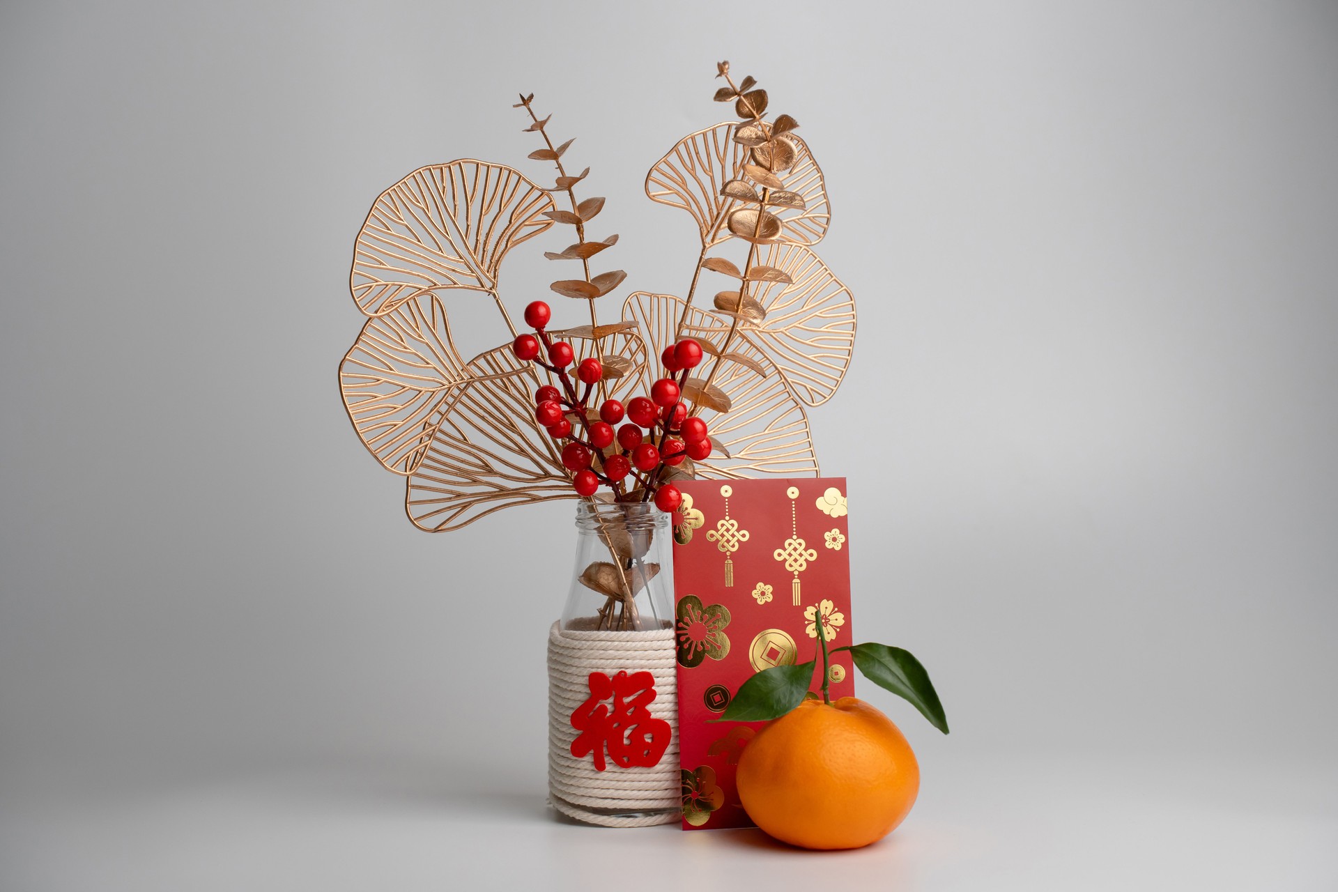 Bouquet of flowers in a vase adorned with a 'Fu' character, accompanied by mandarin and red packet (angpao) for Chinese New Year celebration.